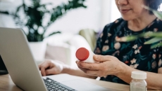   A person holding a pill bottle while using a laptop.