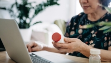 Person holding a pill bottle while sitting and looking at a computer