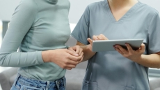 A nurse holding a digital tablet assisting a patient with their records