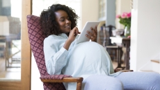 A pregnant person sitting in a chair while looking at a tablet
