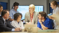 People sitting and standing around a table looking at a computer