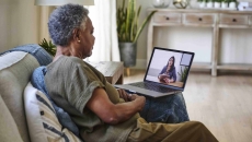 Person sitting on their couch in their home while talking to a telehealth provider on their computer