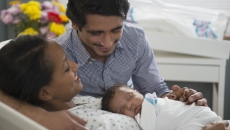 Two people, one lying in a hospital bed and the other leaning over the bed, with both looking at a baby