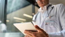 Doctor holding a tablet while in a lab coat with a stethoscope around their neck