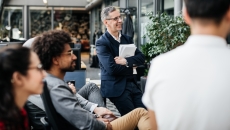 Numerous individuals sitting in a half circle looking at something off-screen