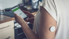 A patient wearing a remote sensor is checking their glucose level from a smartphone