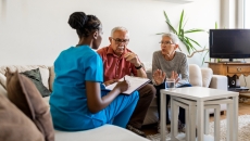 Healthcare provider in scrubs sitting on a couch in a living room with two people