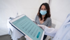 Person holding tablet in front of person wearing surgical mask