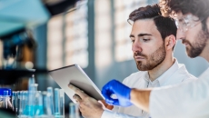 Two scientists in a laboratory setting looking at a piece of paper near some beakers