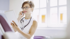 Healthcare provider wearing a stethoscope around their neck while looking at a tablet