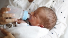 Person holding another small person while feeding them with a bottle