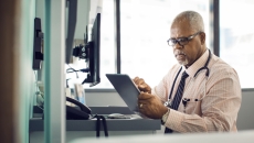 Physician sitting at their desk while looking at a tablet