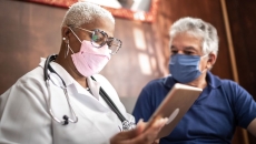 A doctor holding a tablet while talking to a patient.