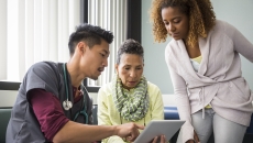 A doctor using a tablet while talking to a patient and her family member.