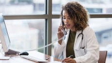 A doctor, sitting in her office, uses the landline to make phone calls regarding patient records.