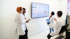 A group of providers or researchers looking at a data dashboard on a large TV on a wall