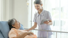 A nurse holding a tablet is taking care of an elderly patient in bed