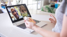 A close up of a woman holding a pill bottle while talking to two providers on her laptop.