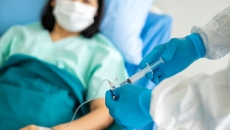 Healthcare provider putting medication into an infusion line with a patient lying in a bed
