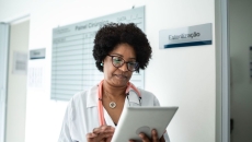Healthcare provider wearing a lab coat and a stethoscope looking at a tablet