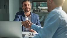 Two people sitting across from each other at a table and shaking hands