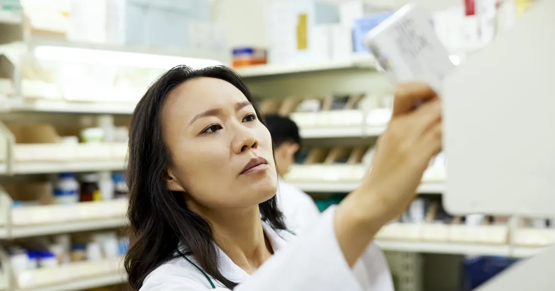 Pharmacist in a pharmacy looking at a piece of paper while holding it up to the light
