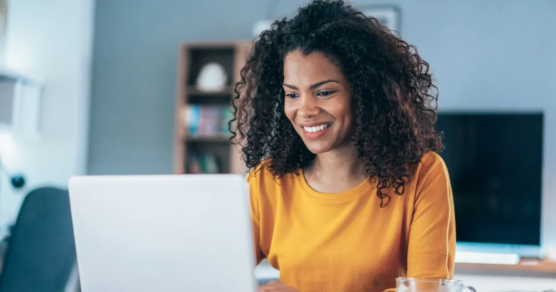 Person sitting in a house looking at a computer and smiling
