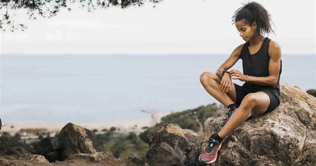 Runner sitting next to the ocean while looking at their smartwatch