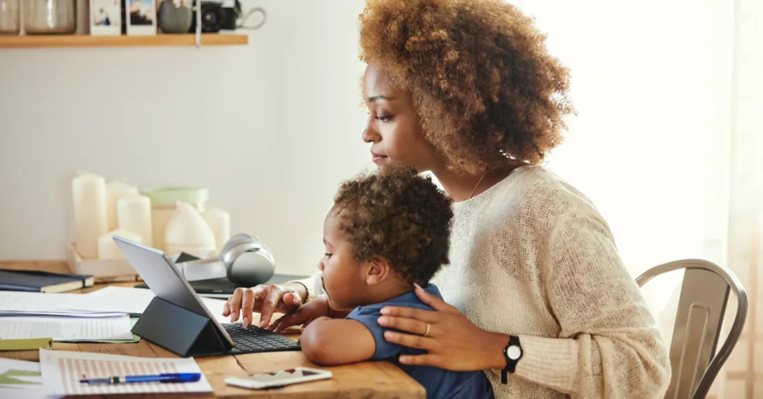 A woman holds a baby while using a tablet
