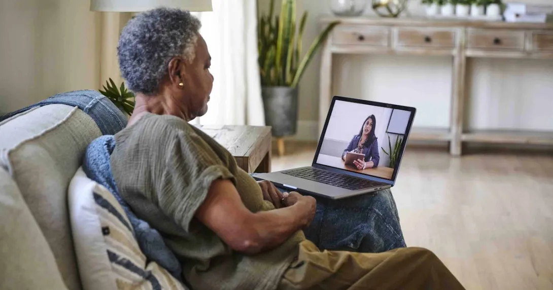Person sitting on their couch in their home while talking to a telehealth provider on their computer