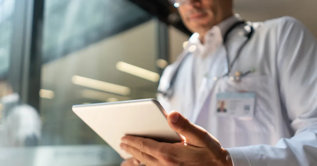 Healthcare provider wearing a lab coat and stethoscope while looking at a tablet