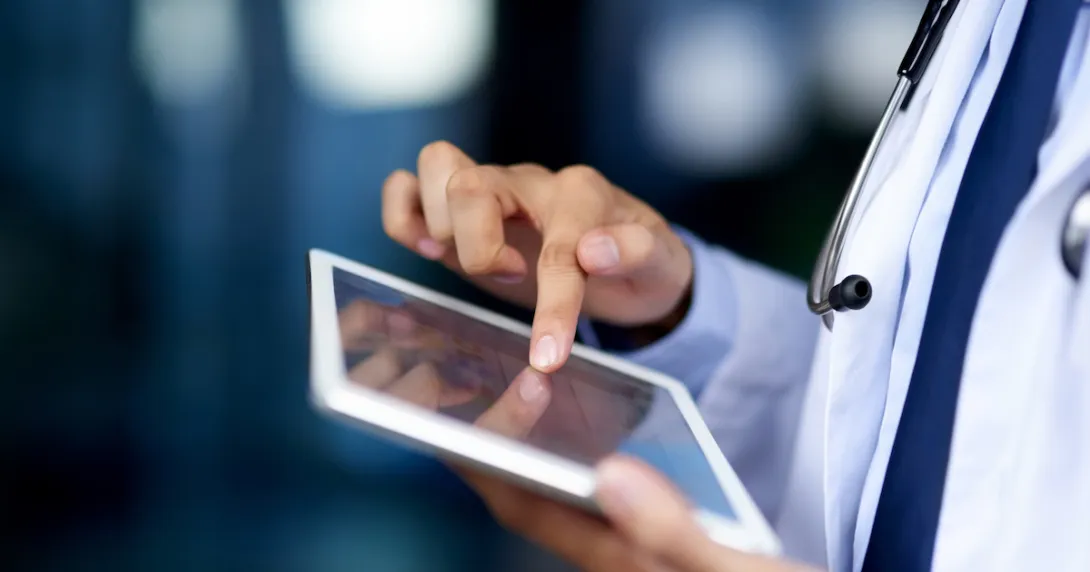 Healthcare provider using a tablet while wearing a white coat and stethoscope