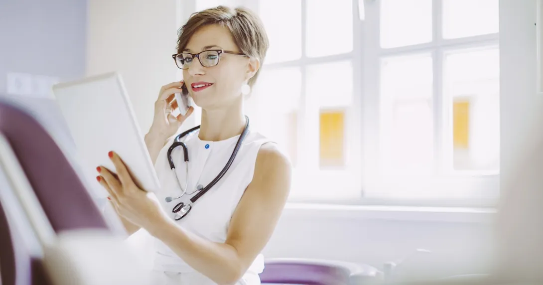 Healthcare provider wearing a stethoscope around their neck while looking at a tablet