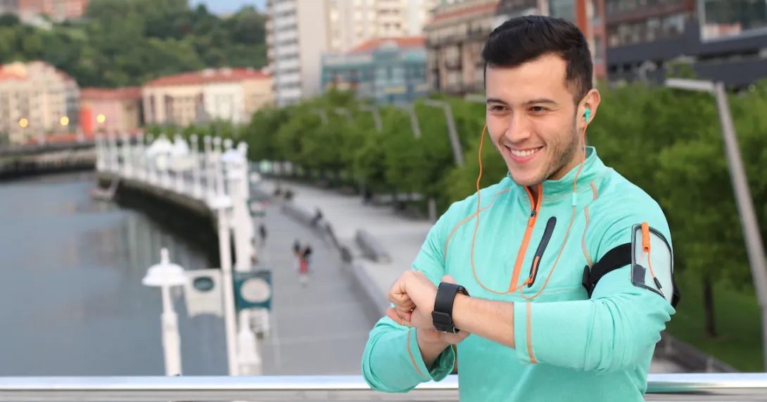 Person wearing a green sweater standing outside looking at a watch
