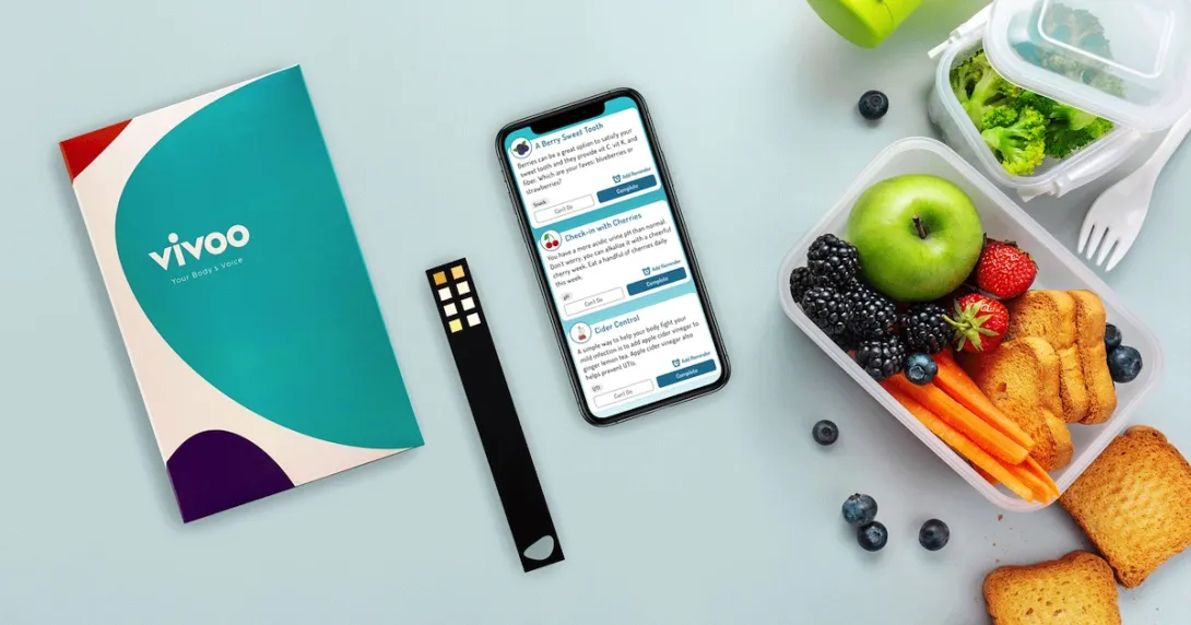 A photo of the Vivoo test kit next to a smartphone and a lunchbox.