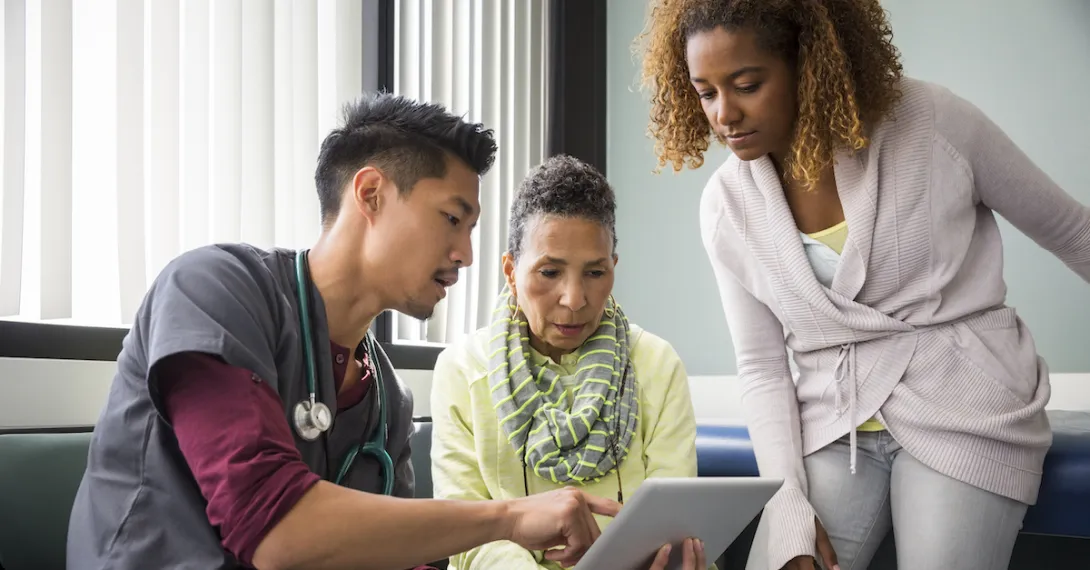 A doctor showing a patient and a family member information on a tablet.