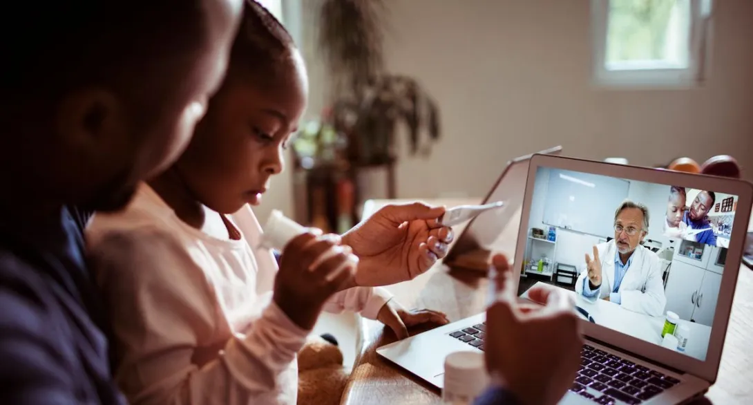 A father and daughter talking to a doctor through a video chat on a laptop.