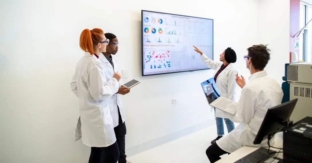A group of researchers looking at data on a television screen.