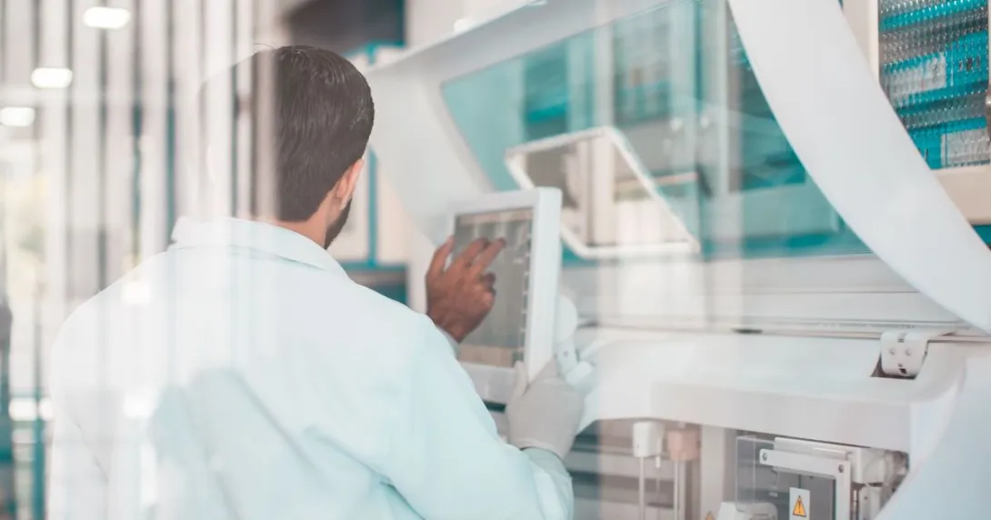 Person standing with their back turned while looking at a computer next while in a lab