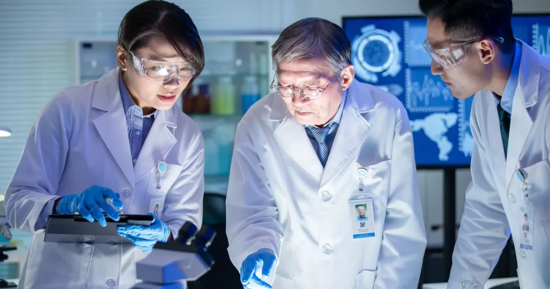 Three healthcare professionals in lab coats looking at something under a light