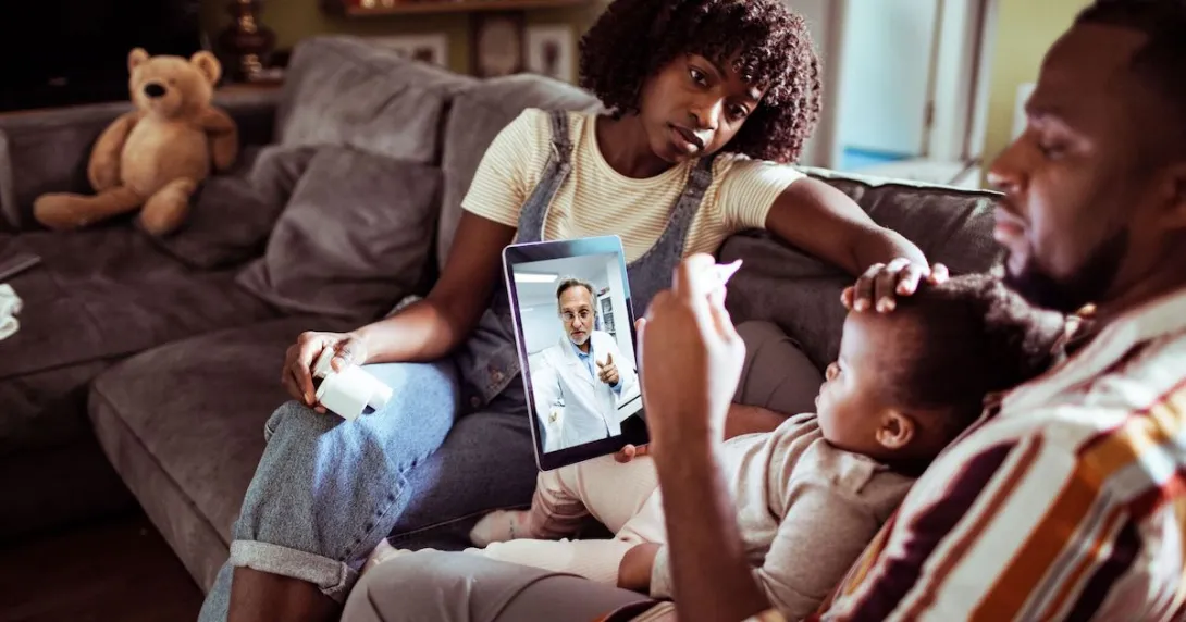 Three people sitting on a couch looking at a computer with a healthcare provider on the screen