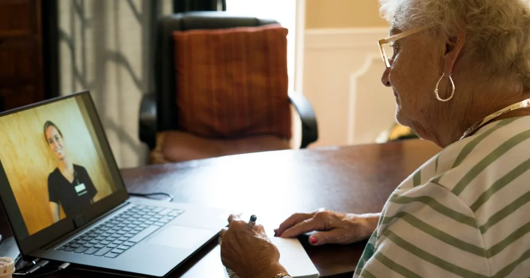 Person sitting at a table with a laptop on it, talking to a healthcare provider via the computer