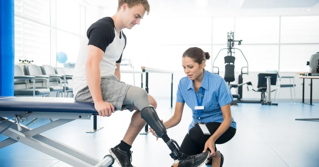 Person with a prosthetic leg undergoing physical therapy with a physical therapist beside them