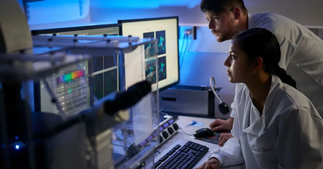 Two healthcare professionals, one sitting down and one standing up, looking at computer screens in a dark room