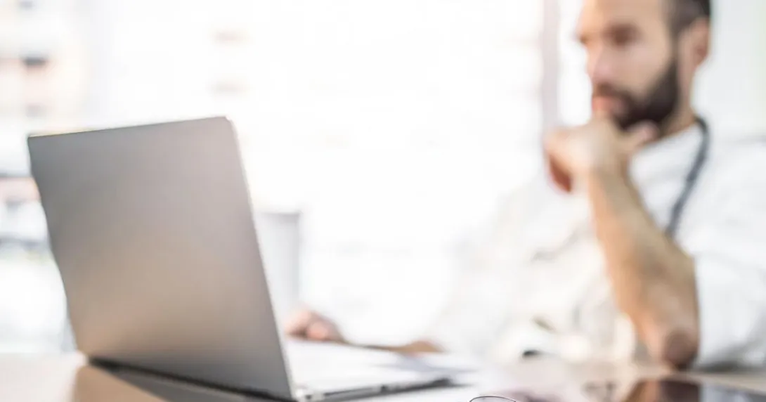 Healthcare provider sitting at a desk while wearing a stethoscope around their neck and looking at a computer