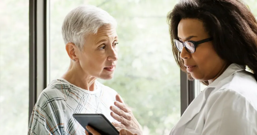 An elderly patient talking to a doctor who is holding a tablet