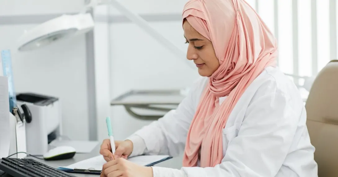 A nurse wearing a hijab filing a patient's form at a desk