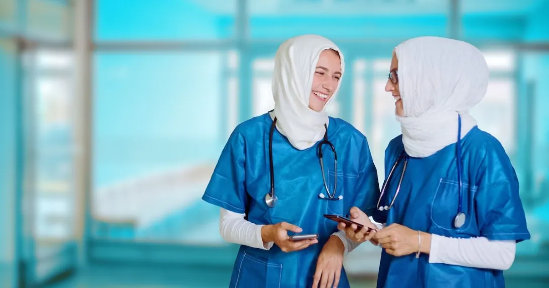 Nurses wearing hijabs conversing while holding their smartphones